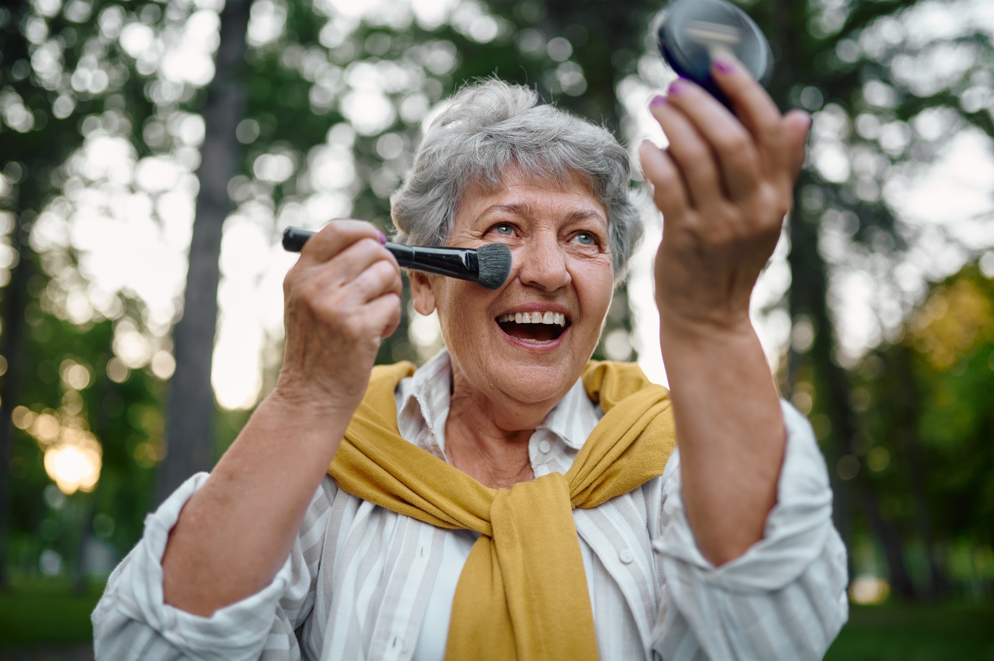 Pretty elderly woman does makeup in summer park